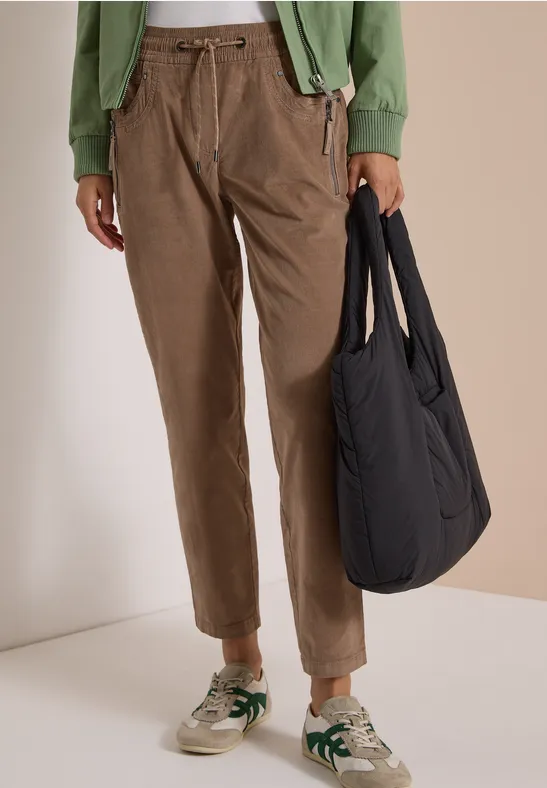 Personne porte un pantalon en velours marron, une veste verte, des baskets beiges à touches vertes et un sac noir.