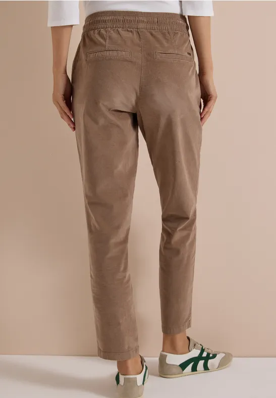 Vue de dos d’une personne portant un pantalon brun clair à taille élastique et des baskets blanches à bandes vertes.