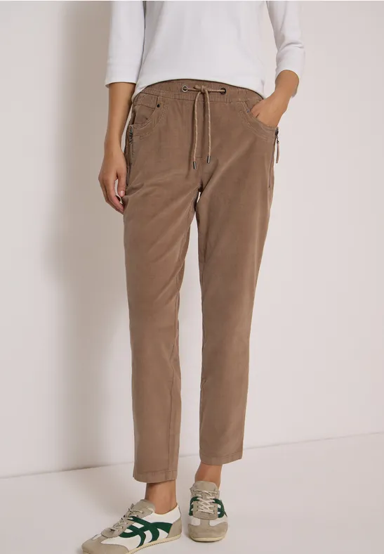 Pantalon ample en velours côtelé beige avec cordon à la taille et baskets décontractées sur fond blanc.