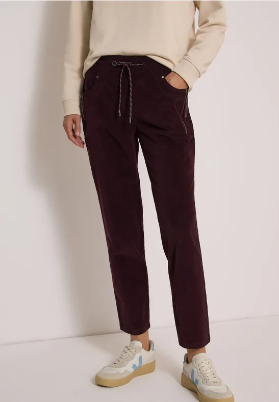 Pantalon en velours côtelé bordeaux à taille élastique, cordon et baskets claires.