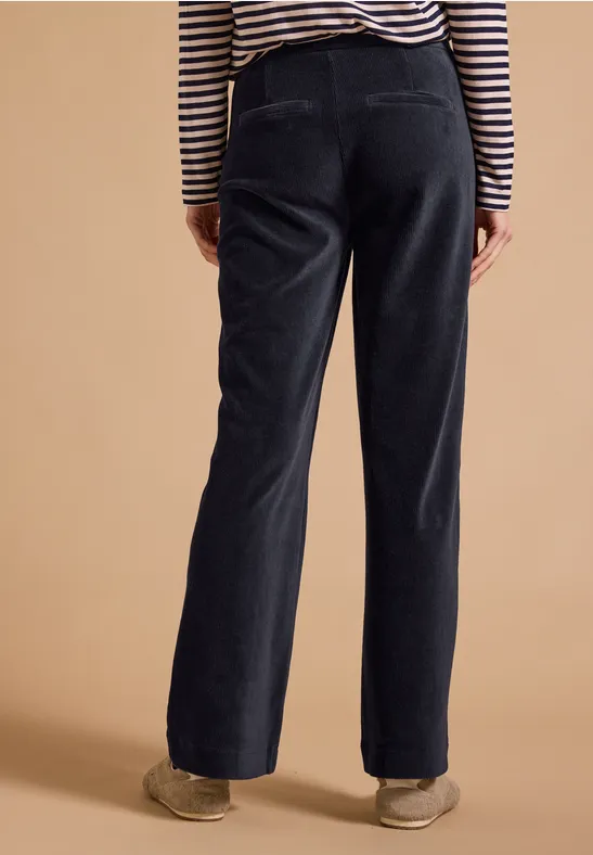 Schwarze, weite Cordhose mit hoher Taille, von hinten fotografiert, kombiniert mit gestreiftem Oberteil und Sneakers.