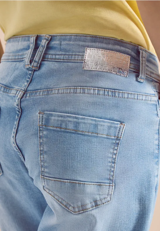Eine Person trägt helle Jeans mit Gesäßtasche und gelbem Oberteil, Perspektive von hinten.