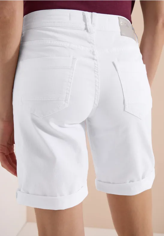Hinteransicht einer Person in weißen, hochgekrempelten Bermudashorts und dunkelrotem Oberteil.