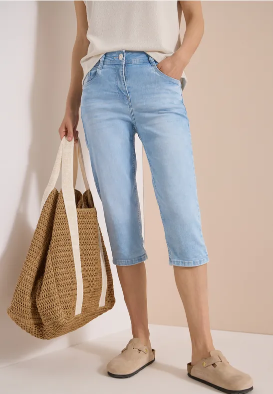 Femme portant un jean capri bleu clair, un haut blanc, un sac en paille et des espadrilles beiges.