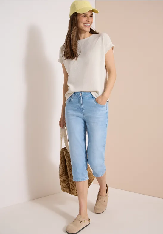 Femme en tenue estivale avec t-shirt beige, capri en jean, sac en paille et mocassins