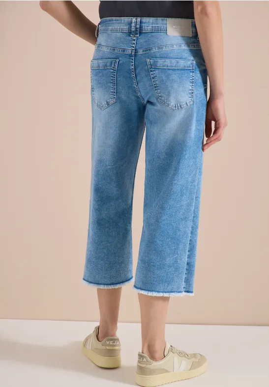 Rückansicht einer Person in hellblauen, weiten Cropped-Jeans mit Fransen und beigen Sneakern