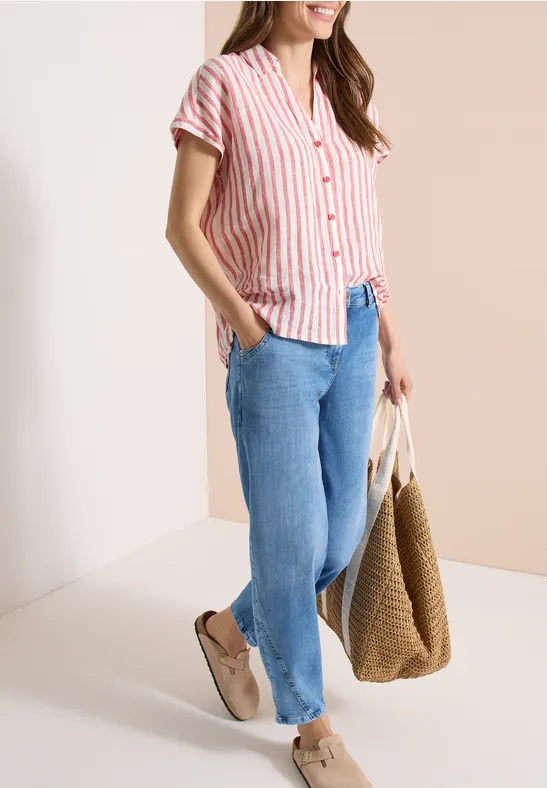 Femme en chemise à rayures, jean bleu, chaussures beiges et grand sac tressé sur fond clair.