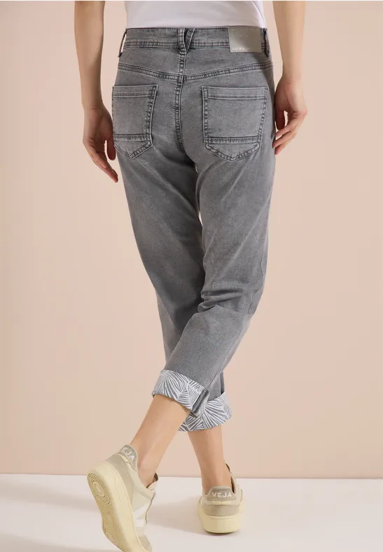 Rückansicht einer Person in grauen, hochgekrempelten Jeans und Sneakern vor neutrem Hintergrund