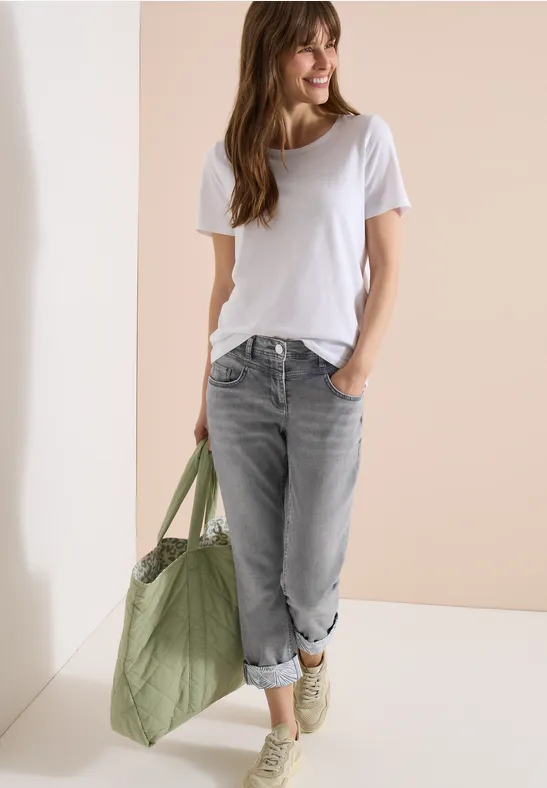 Frau trägt weißes T-Shirt, graue Jeans, olivgrüne Tasche und weiße Sneaker.