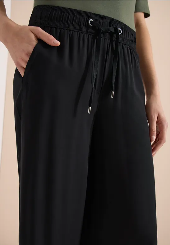 Pantalon noir ample en tissu, taille élastique avec cordons et poches.