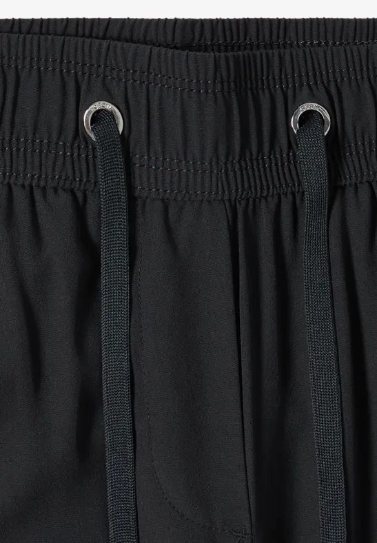 Nahaufnahme eines schwarzen Hosenbunds mit Gummizug und schwarzen Kordeln durch Metallösen.