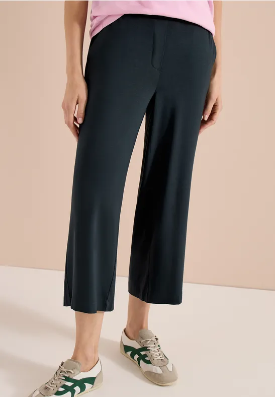 Schwarze, weite Cropped-Hose bis zum Knöchel kombiniert mit lässigen Sneakers.