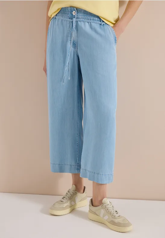 Locker sitzende, hellblaue, weite Jeans mit Kordelzug bis knapp über die Knöchel, kombiniert mit beigen Sneakern.
