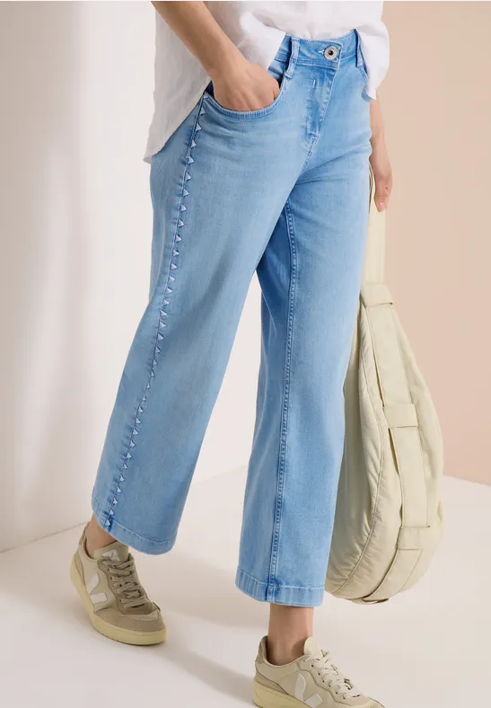 Helle, gerade geschnittene Jeans mit Zierknöpfen an den Seiten, kombiniert mit beigen Sneakers und Tasche.