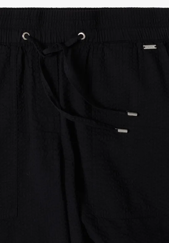 Pantalon noir à structure gaufrée, taille élastique et cordon avec embouts argentés.