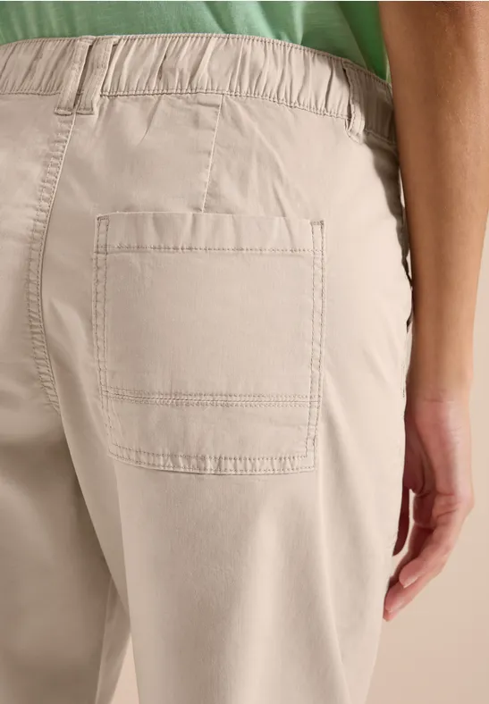 Vue de dos : personne en pantalon beige avec poche plaquée, haut vert visible.