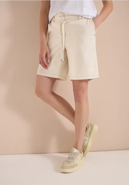 Person trägt weißes T-Shirt, kniehohe beige Shorts und helle Sneaker.