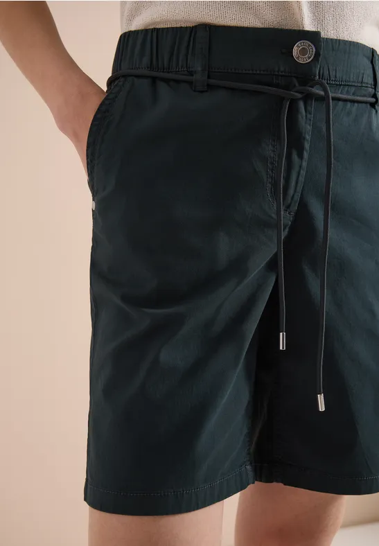 Nahaufnahme von dunkelgrünen Bermudashorts mit Kordelzug und Hosentaschen, Hand in der Tasche.