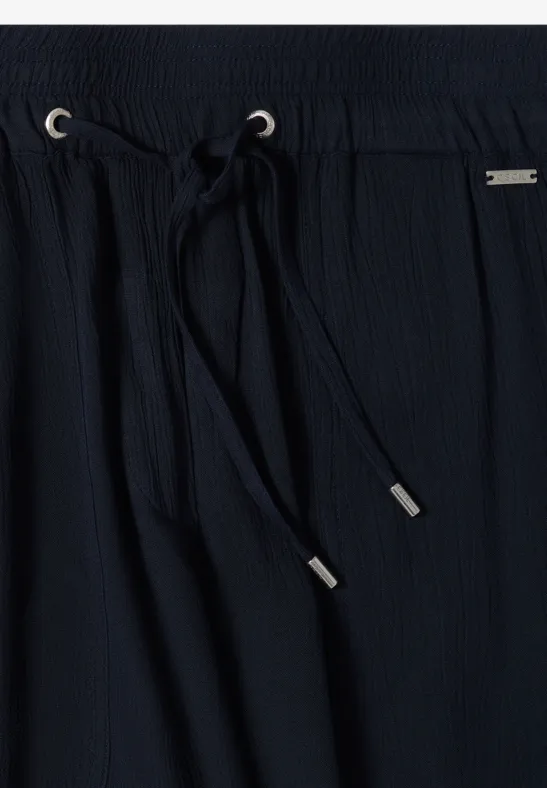 Nahaufnahme einer schwarzen, texturierten Hose mit elastischem Bund und Kordelzug mit silbernen Enden.