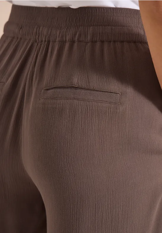 Nahaufnahme brauner, strukturierter Hose mit elastischem Bund und einer Gesäßtasche.