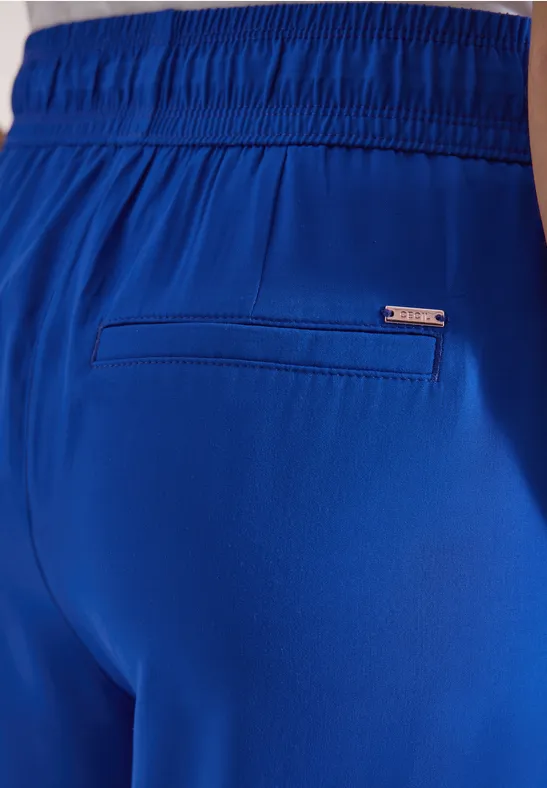 Nahe Ansicht einer blauen Shorts mit elastischem Bund, Leistentasche und kleinem Markenlogo.