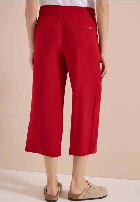 Rote, weite 7/8-Hose mit Gummibund und Gesäßtasche, kombiniert mit beigen Slippern.