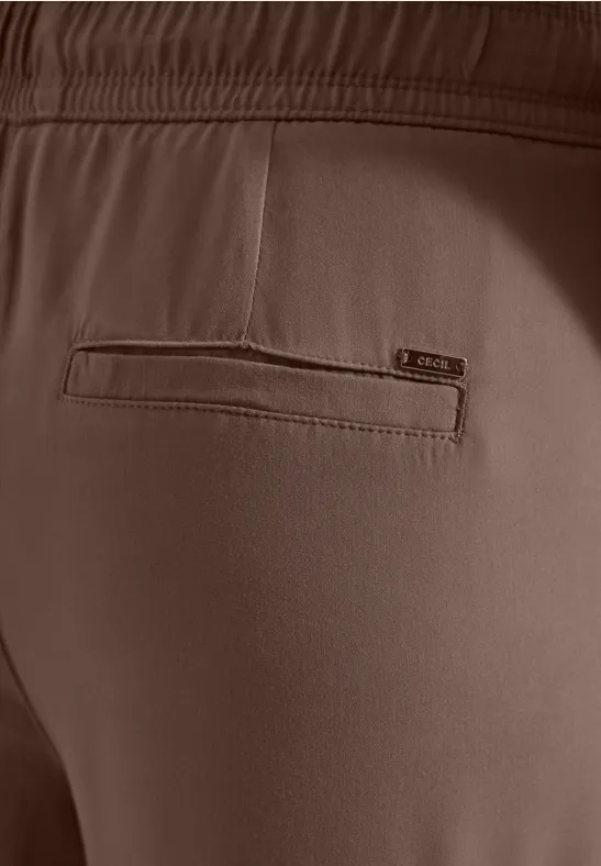 Nahaufnahme der Rückseite einer braunen Hose mit elastischem Bund und eingearbeiteter Tasche mit Reißverschluss.