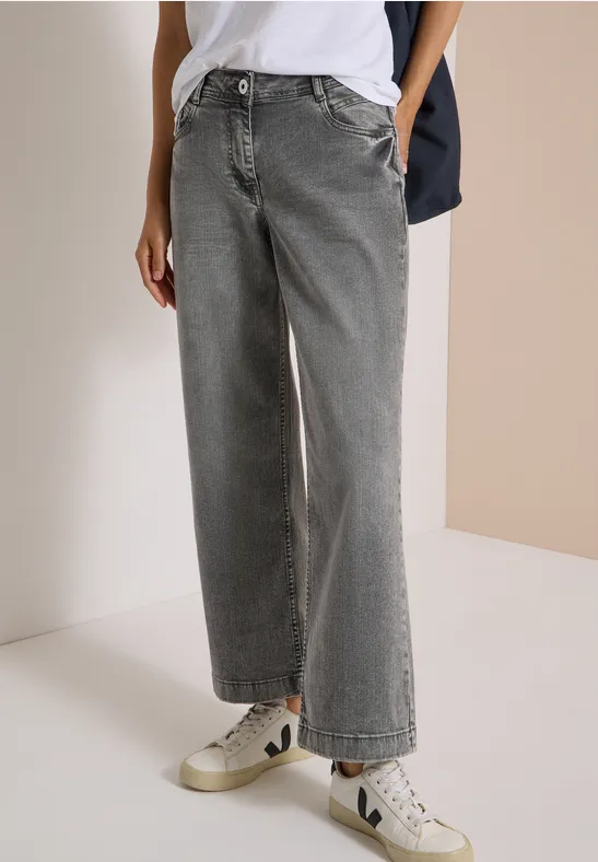 Ein Model trägt weite, graue High-Waist-Jeans und weiße Sneaker.