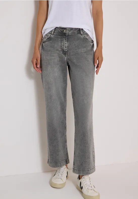 Eine Person trägt gerade geschnittene graue Jeans, weißes T-Shirt und weiße Sneaker.