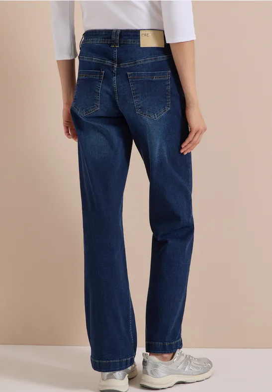 Vue de dos d'une personne portant un jean large bleu foncé et des baskets blanches sur fond beige.