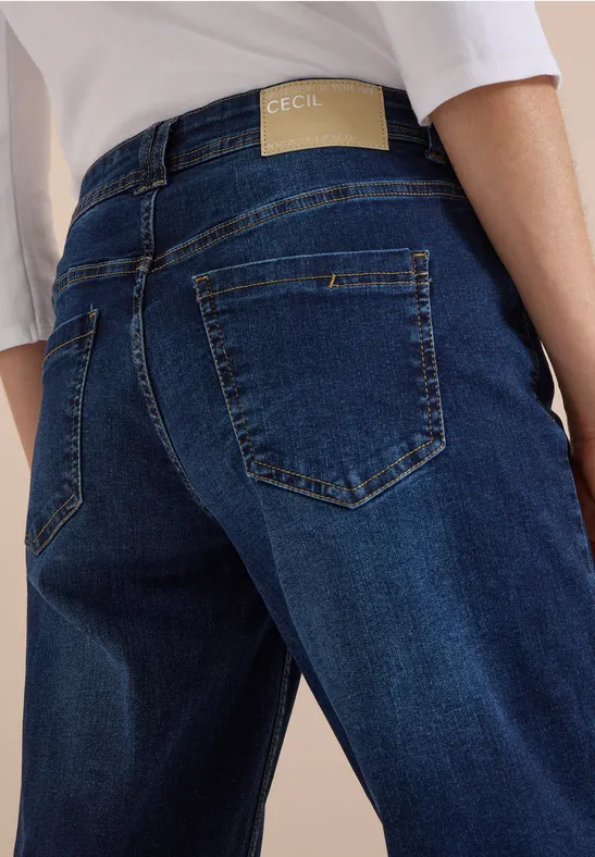 Vue arrière d’une personne en jean bleu avec étiquette discrète et haut blanc.