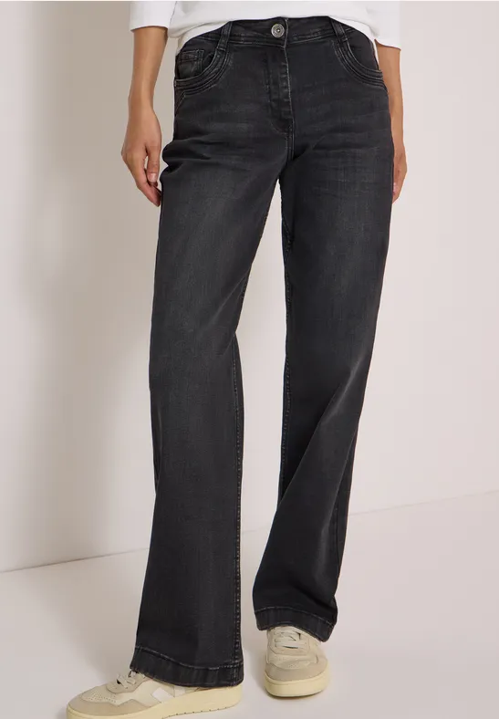 Jeans noirs à coupe droite portés avec des baskets blanches sur un modèle debout.