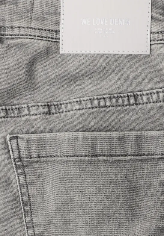 Gros plan d’un jean gris vu de dos avec poche arrière, passants de ceinture et étiquette « WE LOVE DENIM ».