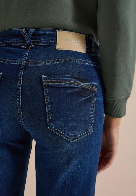 Une personne porte un jean bleu foncé et un sweat vert, vue de dos.