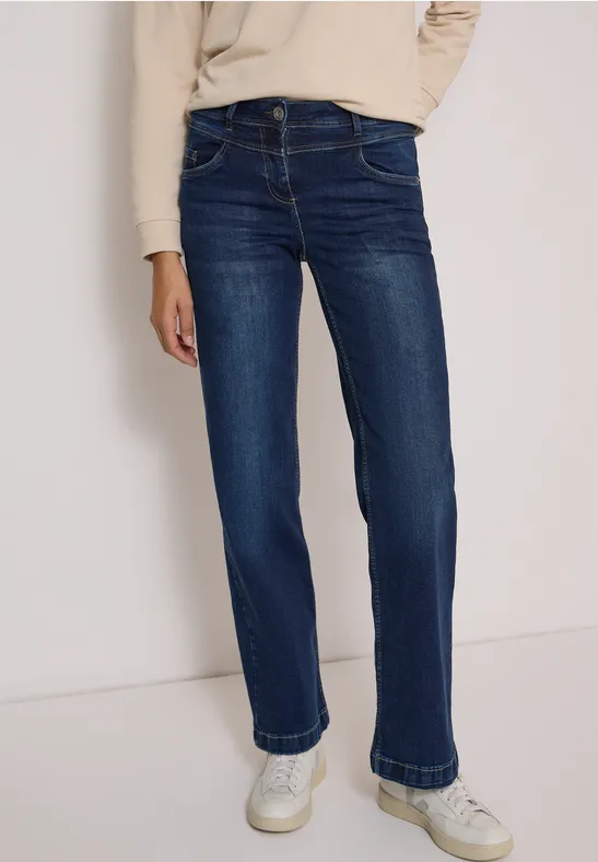 Une personne porte un jean droit bleu foncé avec des baskets blanches.