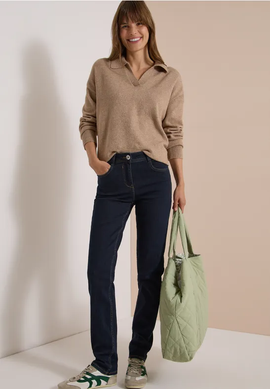 Frau in beigem Pullover, Jeans und grünen Sneakers, trägt eine große gesteppte grüne Tasche.