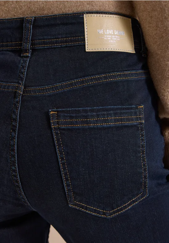 Rückenansicht in dunkler Jeans mit Gesäßtasche, beigefarbenem Label und braunem Mantel.