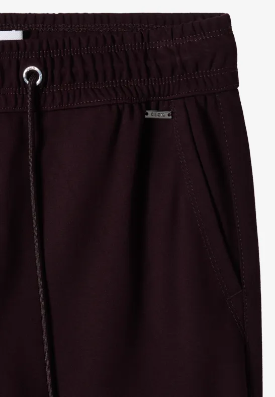 Nahaufnahme einer dunkelroten Jogginghose mit elastischem Bund, Tunnelzug und seitlicher Tasche.