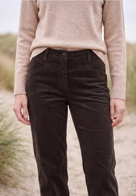 Personne debout sur la plage devant les dunes, portant un pull beige et un pantalon en velours côtelé noir