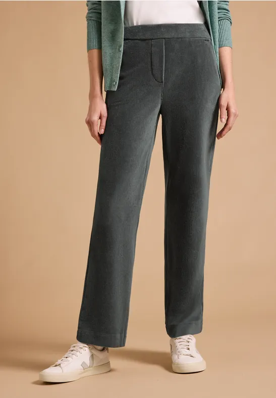 Frau trägt dunkelgraue Cordhose mit geradem Schnitt, Seitentaschen und weißen Sneakers.