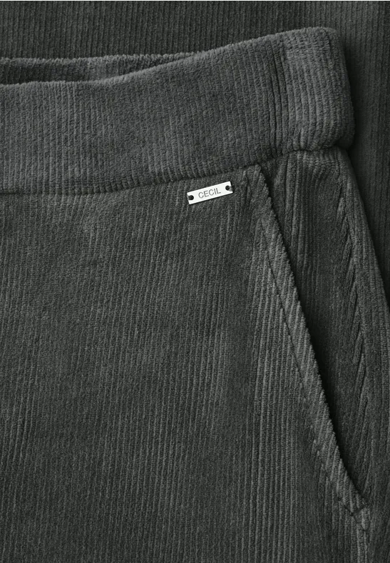 Detailaufnahme einer grauen Cordhose mit elastischem Bund und seitlicher Tasche mit kleinem Metallschild.