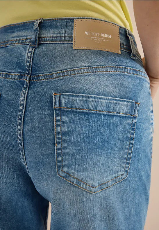 Rückansicht einer Person in blauen Jeans mit Gesäßstasche und Markenetikett, gelbes Oberteil erkennbar.