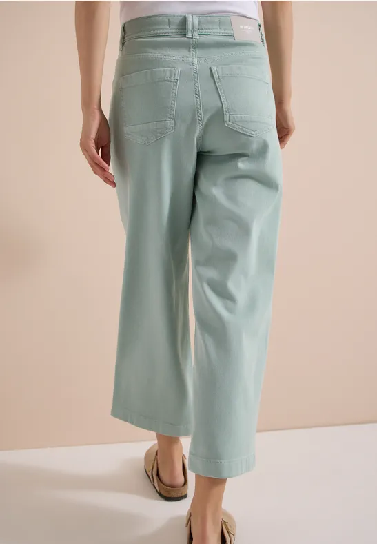 Modell von hinten in pastellgrünen, weiten 7/8-Hosen und flachen Sandalen.