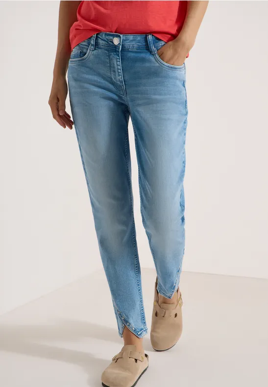 Helle Jeans mit V-Saum und beigen Wildleder-Slippern, rotes Oberteil teils sichtbar.
