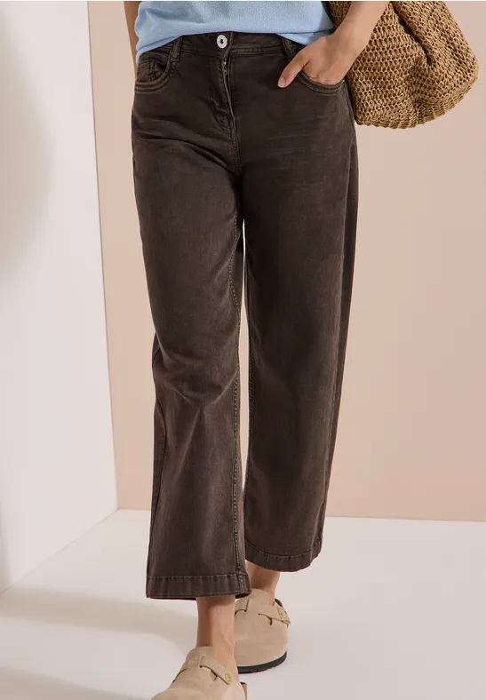 Femme portant un pantalon large en velours côtelé marron foncé, mocassins blancs et sac en paille.