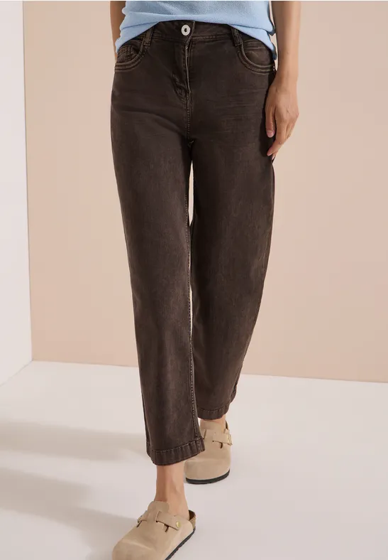 Une personne porte un jean taille haute noir et des chaussures beiges confortables sur fond neutre.