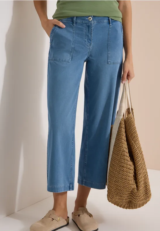 Femme en jean large et court, haut vert, sac en osier et mules beiges.