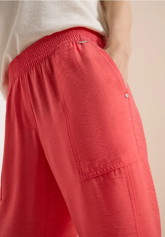 Locker sitzende, rote Stoffhose mit elastischem Bund und aufgesetzter Seitentasche, weich fallend.