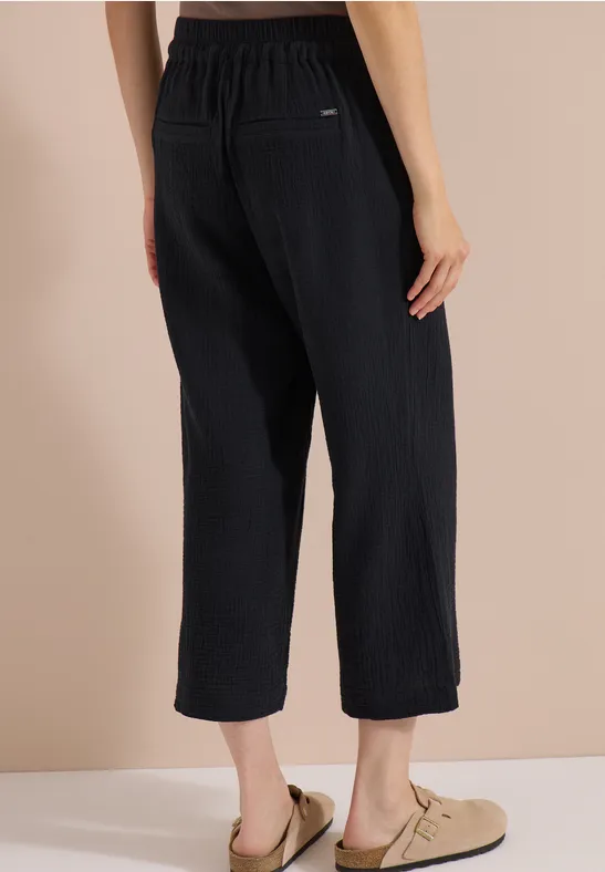 Vue de dos: pantalon en maille côtelée noir, ample et court, taille élastique, mocassins beiges.