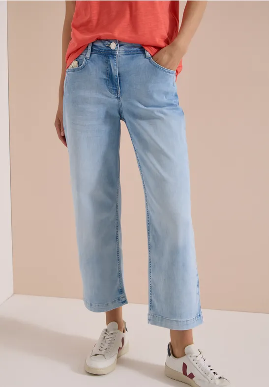Modische, hellblaue, weit geschnittene Jeans bis zur Knöchelhöhe, kombiniert mit weißen Sneakers.